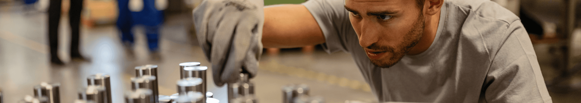 Close-up of a man with work gloves tightening screws inside a factory