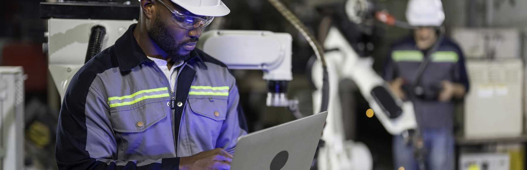 Man in hard hat reviewing info on a laptop in a manufacturing facility