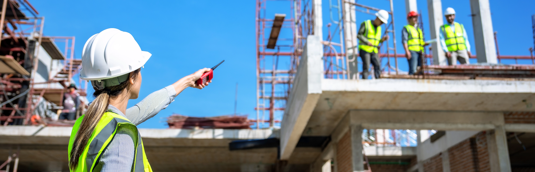 Woman in white hard hat pointing toward three men at a construction site