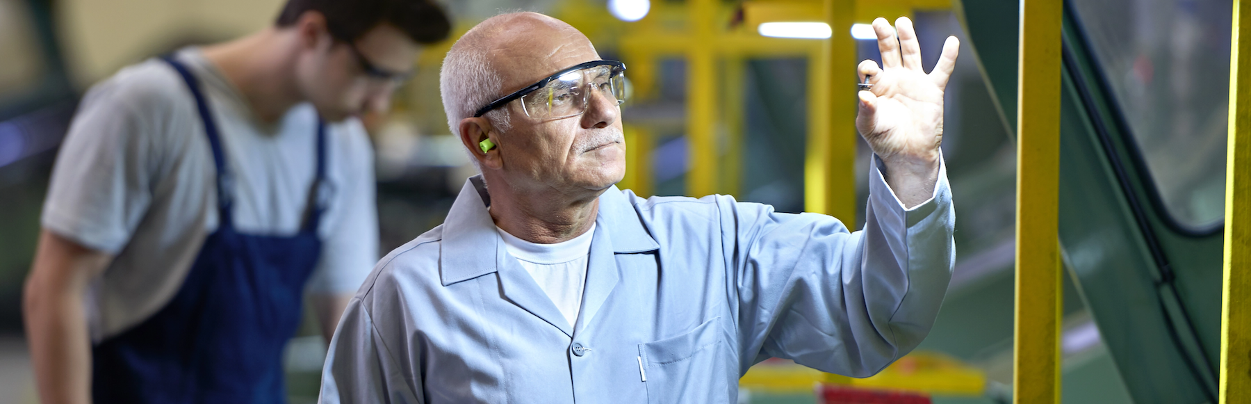 Man in safety goggles holding a bolt in his left hand to inspect it