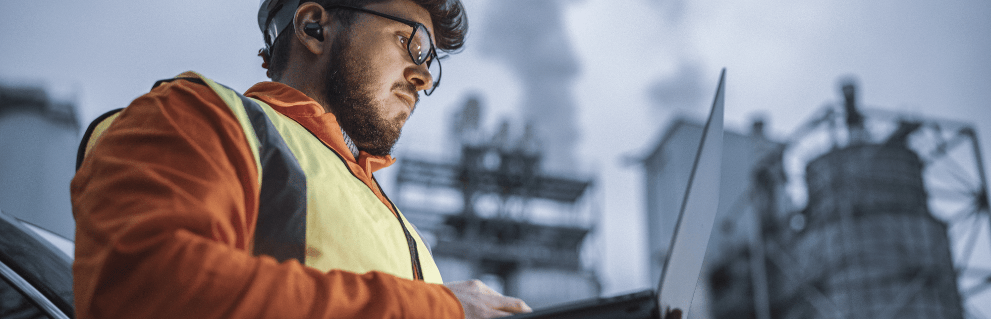 Man in glasses and a yellow safety vest on a laptop at a construction site