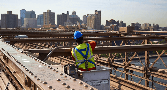 Man in blue hard hat working at a construction site with a city skyline in the background