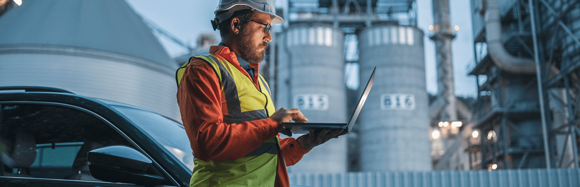 Man in hard had and safety vest standing with a laptop at a worksite